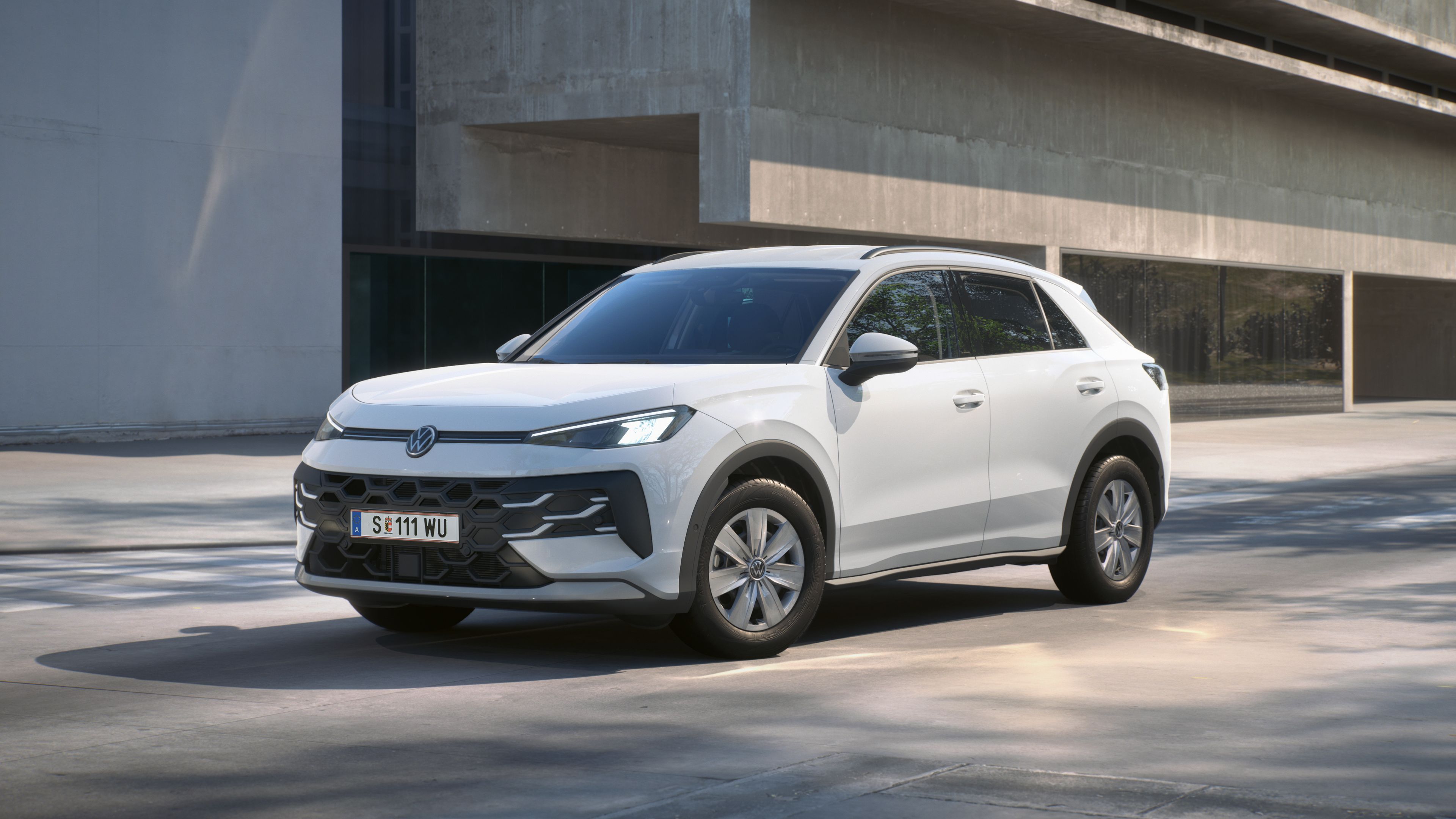 Ein weißer Volkswagen T-Roc R Trend steht in 3/4-Frontansicht vor einem Gebäude.