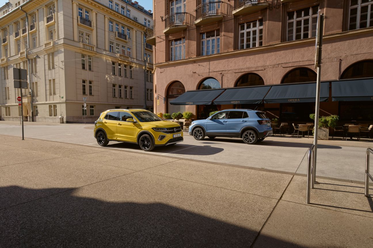 Ein gelber und ein blauer VW T-Cross fahren auf einer Straße aneinander vorbei.