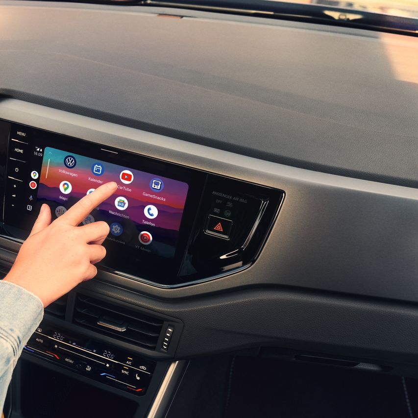 Eine Hand wählt ein App-Symbol im Menü des Infotainment-System eines VW Polo aus.