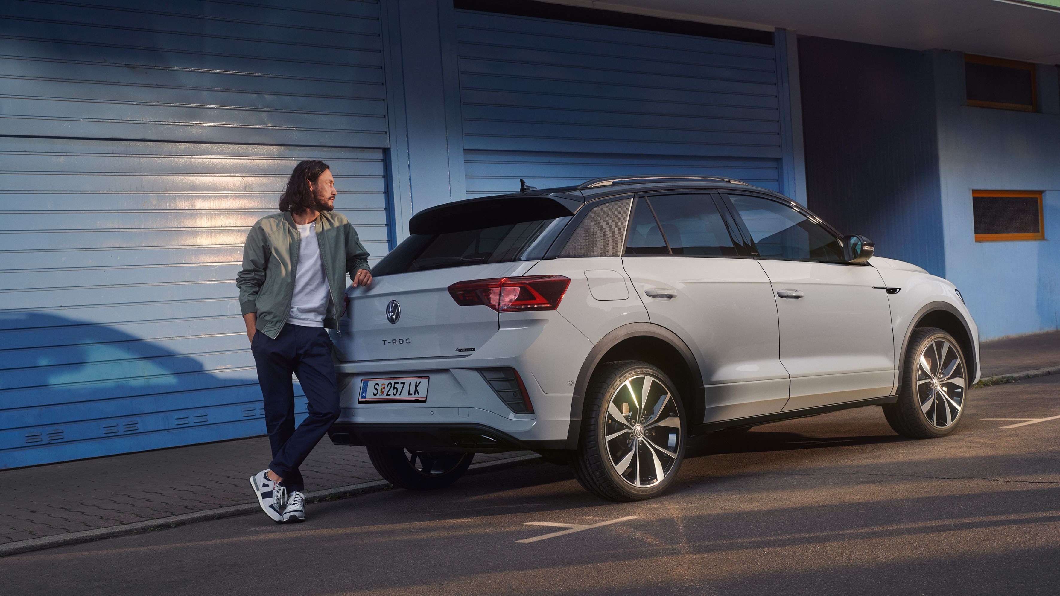 Ein Mann lehnt am Heck eines weißen T-Roc, der am Straßenrand parkt.