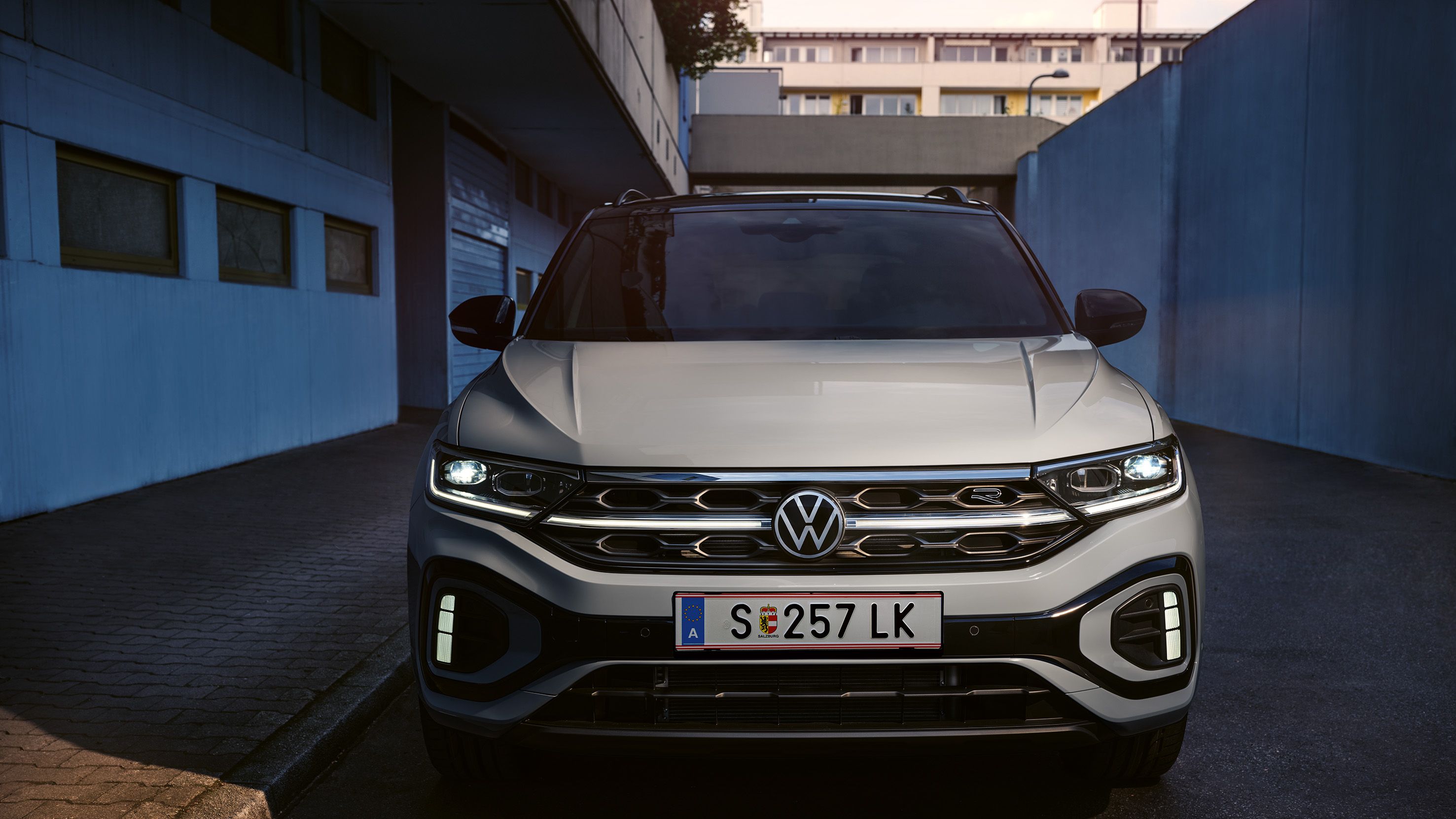 VW T-Roc R-Line Front in Weiß, LED-Tageslichtscheinwerfer und das optionale, illuminierte Kühlerschutzgitter leuchten