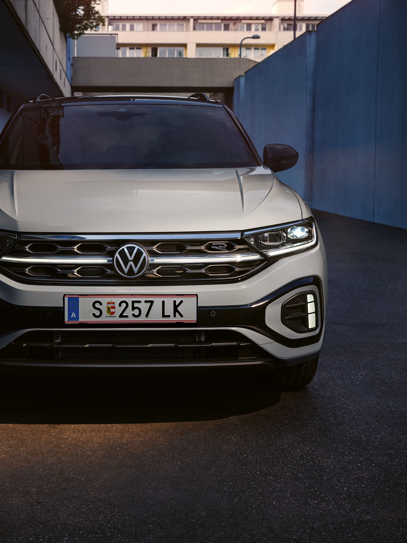 VW T-Roc R-Line Front in Weiß, LED-Tageslichtscheinwerfer und das optionale, illuminierte Kühlerschutzgitter leuchten