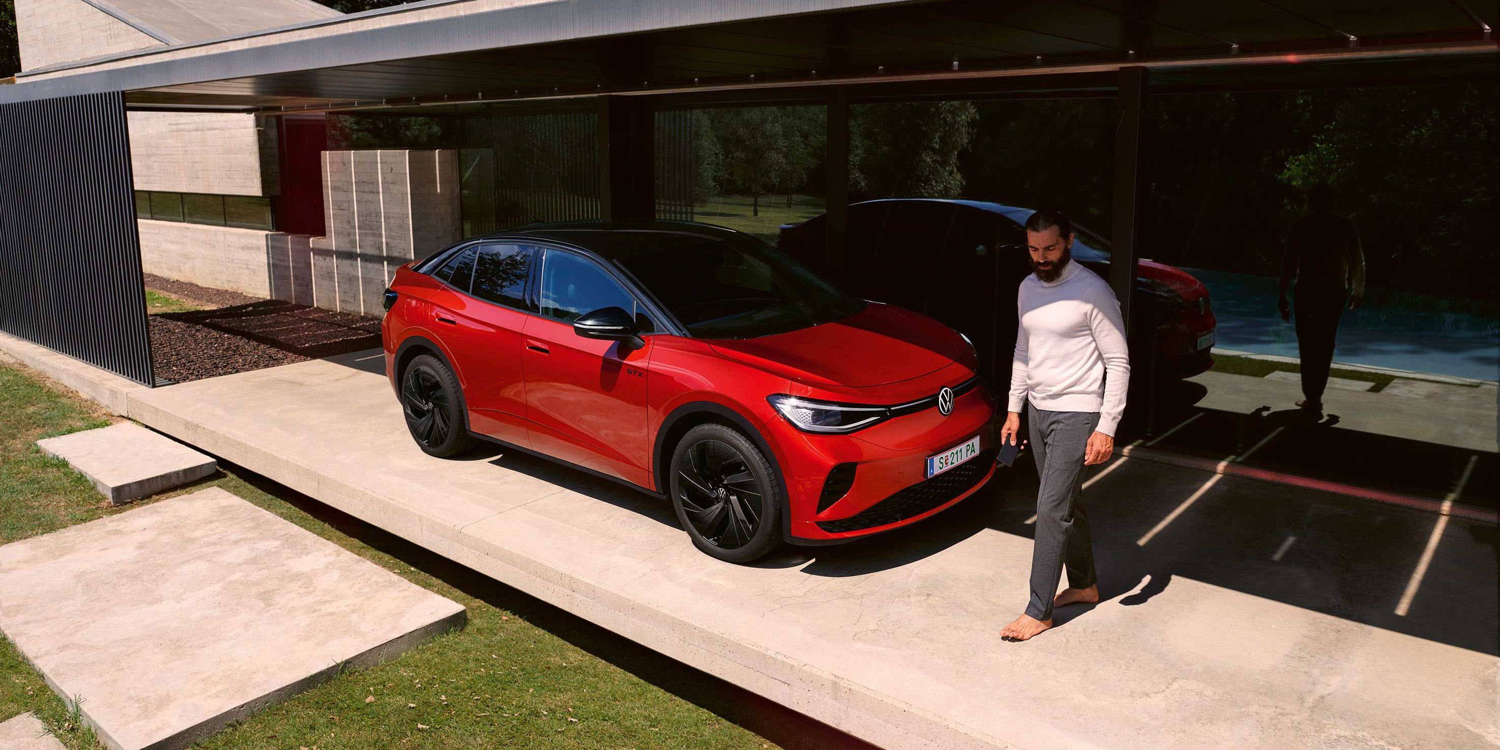 Roter VW ID.5 GTX von schräg vorne in einem modernen Carport, ein Mann geht vor der Motorhaube entlang