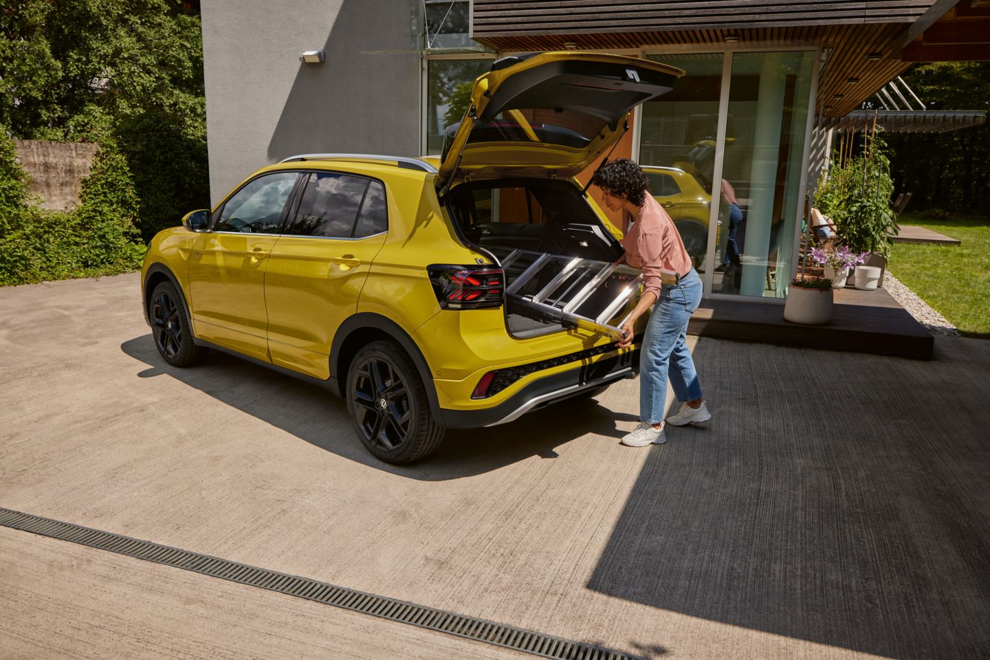 Eine junge Frau schiebt eine Leiter in den Kofferraum eines gelben VW T-Cross.