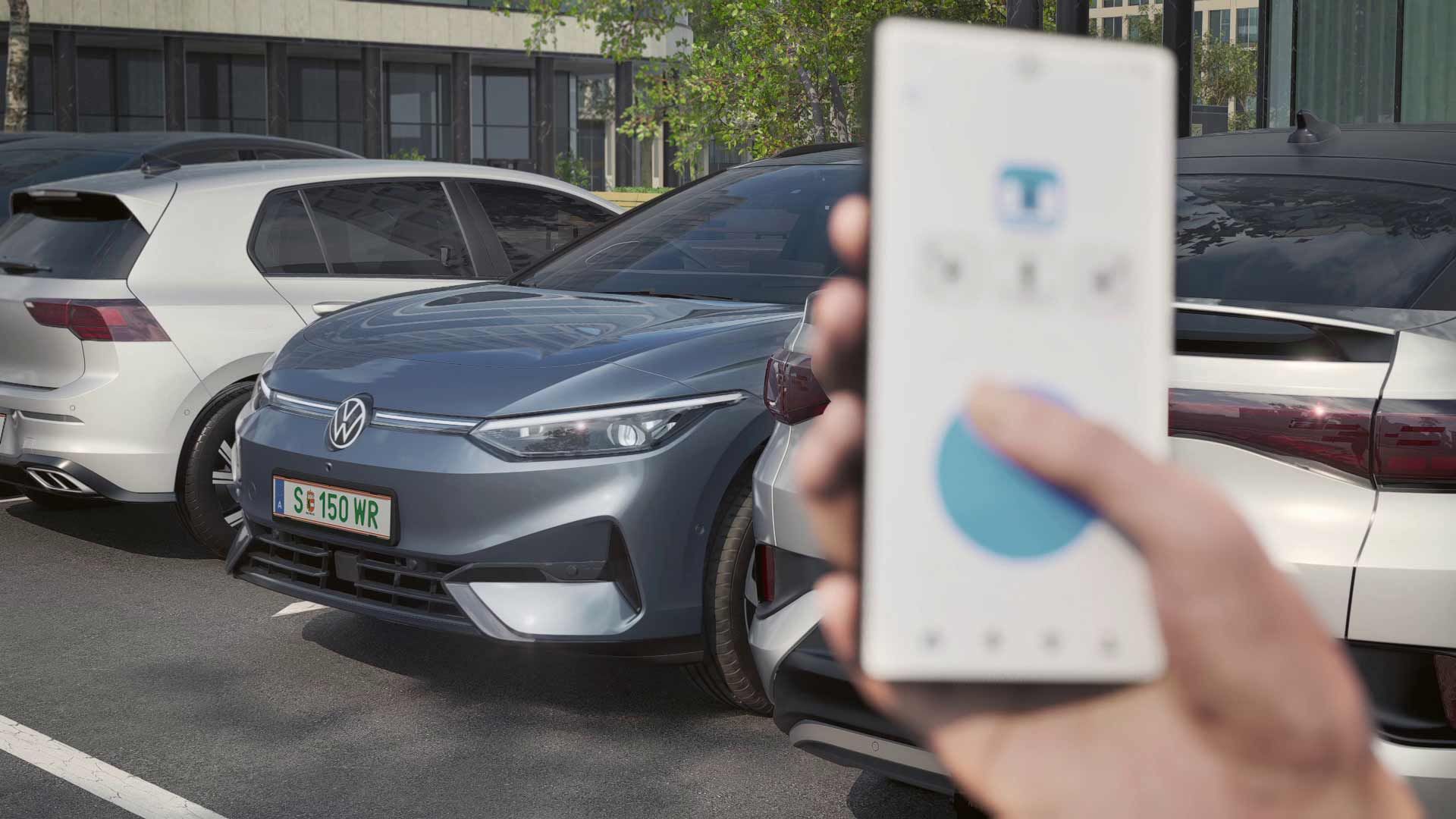 Eine Person hält ein Smartphone in der Hand und steuert damit ein graues Elektroauto von Volkswagen, das zwischen zwei anderen Autos geparkt ist. Das Auto scheint aus einem Parkplatz herauszufahren. Im Hintergrund sind moderne Gebäude zu sehen.