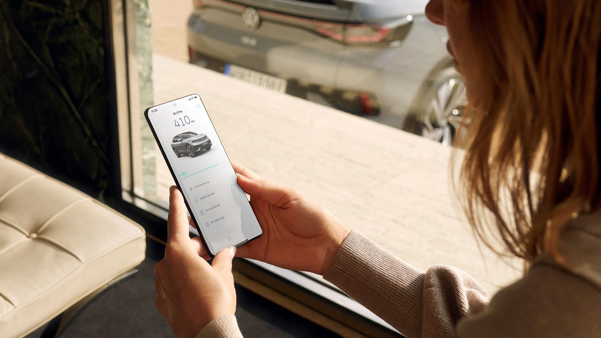 Heckansicht eines grauen VW ID.5, im Vordergrund bedient eine Frau ein Smartphone