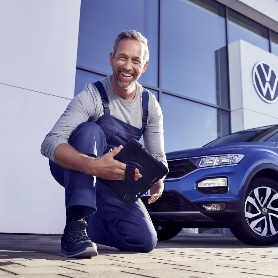 Ein Volkswagen Service Techniker mit Tablet, kniet vor einem blauen Volkswagen T-Roc