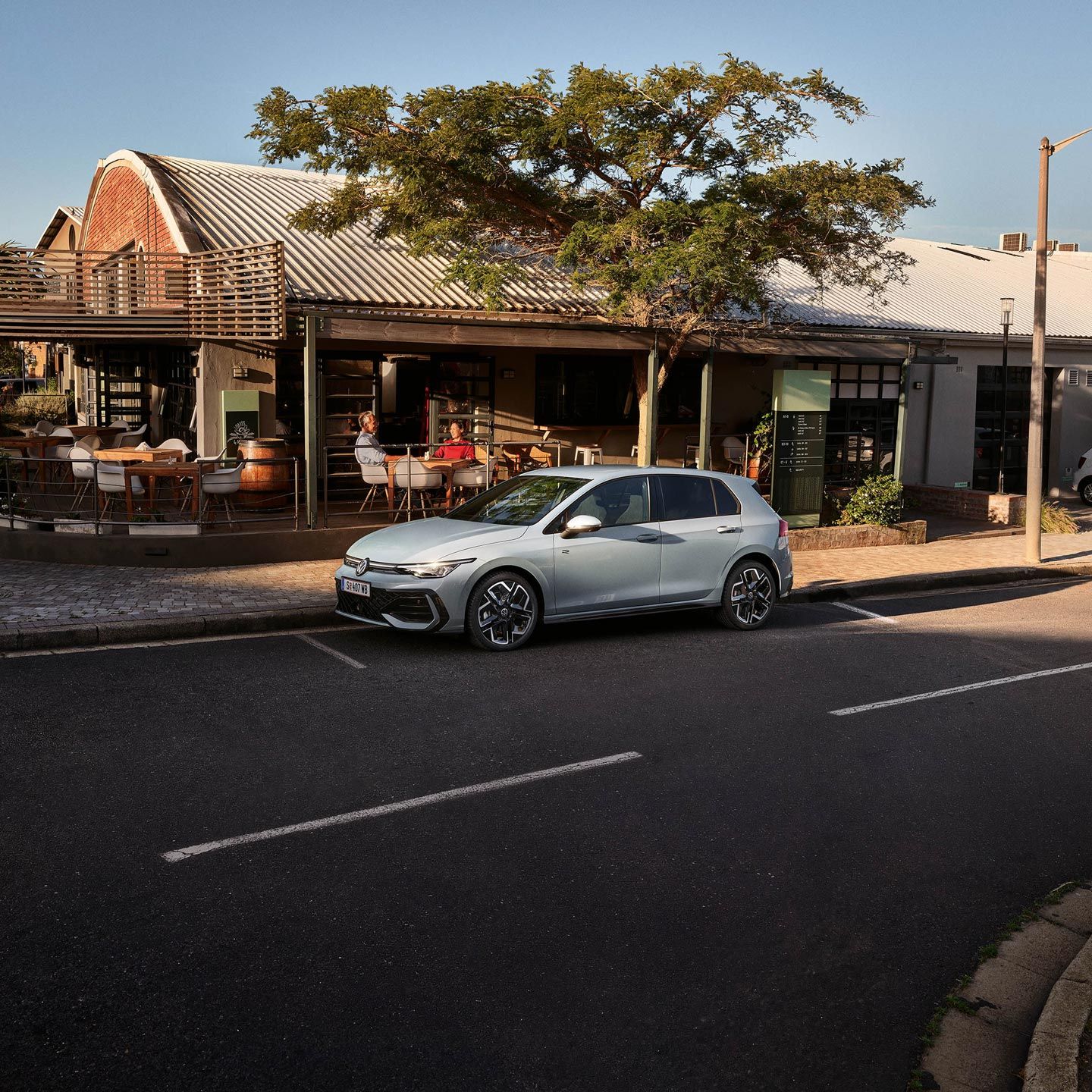 Weißer Golf R-Line parkt seitlich vor einem Restaurant.