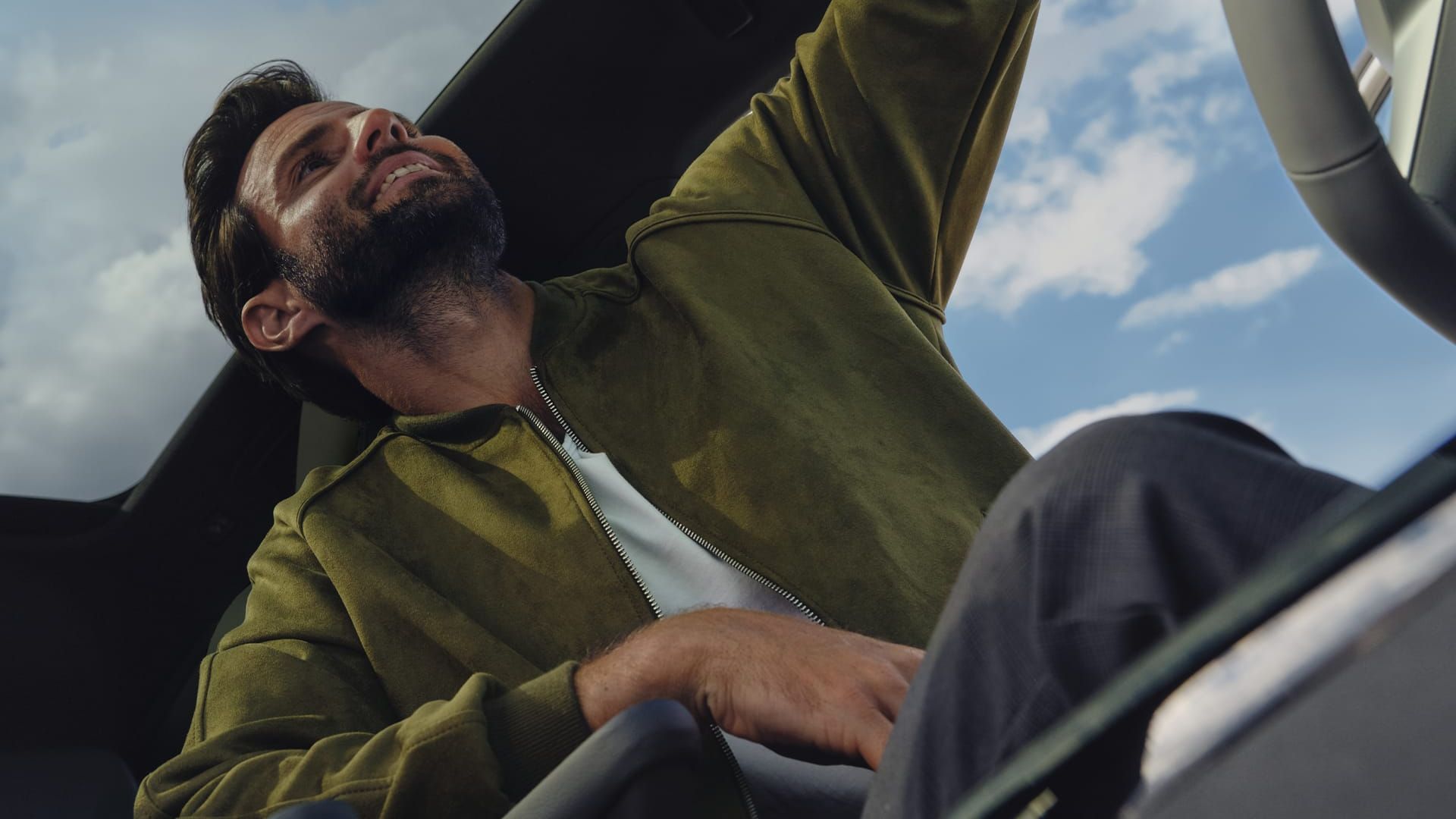 Blick von unten ins Cockpit des VW ID.4 mit Panoramaglasdach, Mann auf Fahrersitz nutzt Bedienelemente in Deckenkonsole