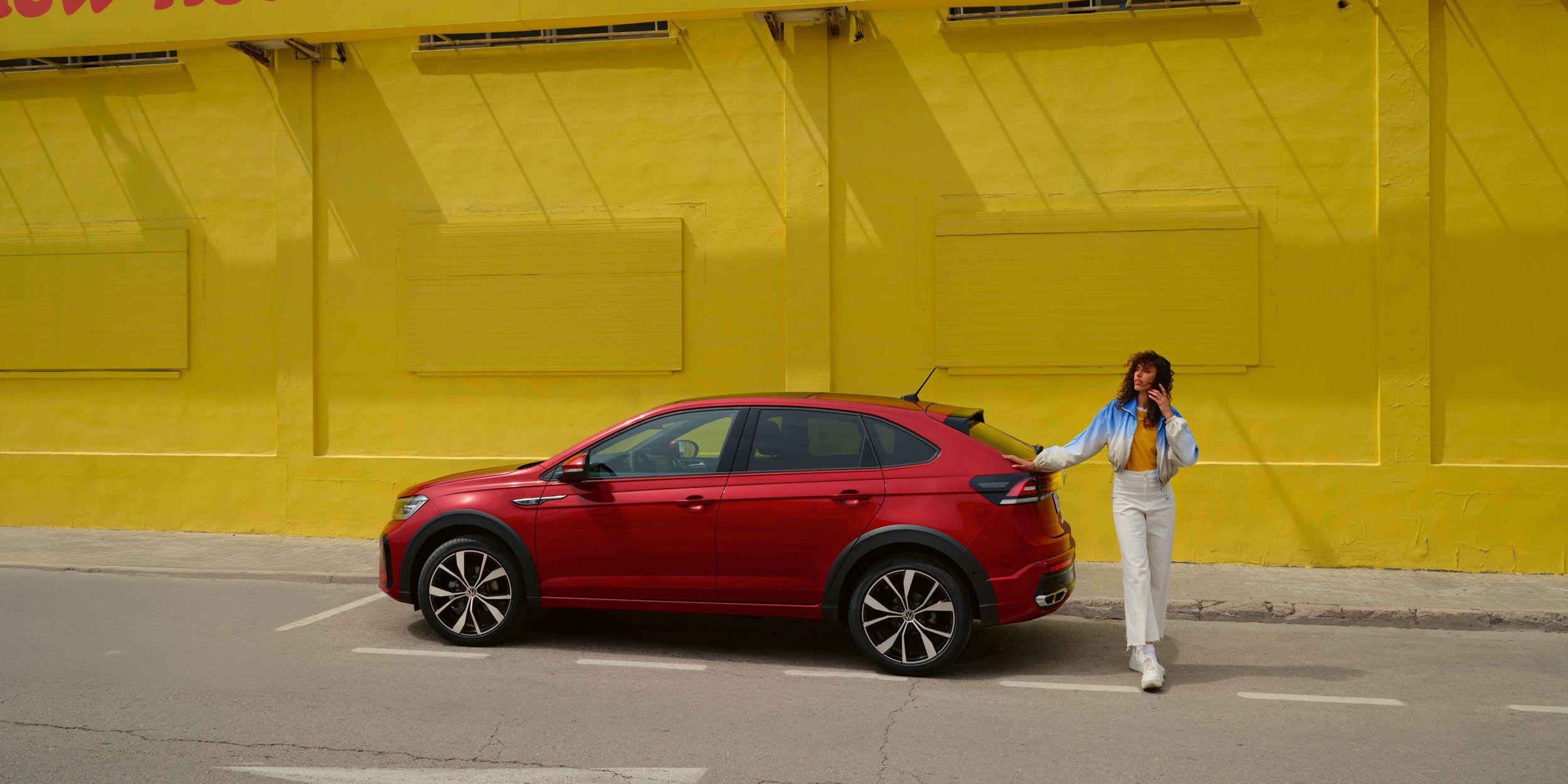 Ein roter VW Taigo steht vor einer gelben Wand auf einer Asphaltierten Strasse.