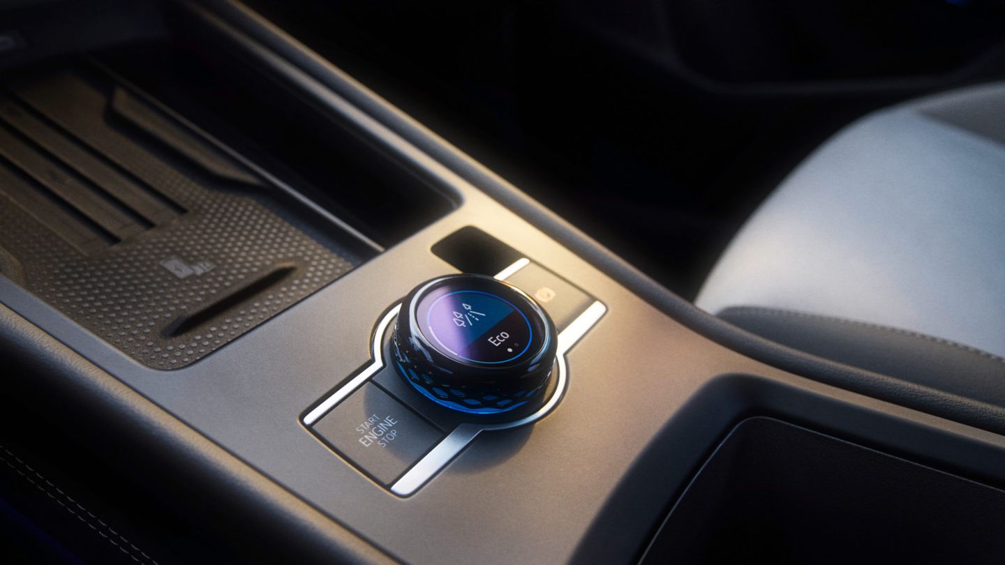 Nahaufnahme einer Mittelkonsole in einem T-Roc mit Fokus auf den Fahrerlebnisschalter. Ein runder Drehknopf mit LED-Anzeigen zur Steuerung verschiedener Fahrzeugfunktionen. Hochwertige Materialien und ein elegantes Design sind zu erkennen.