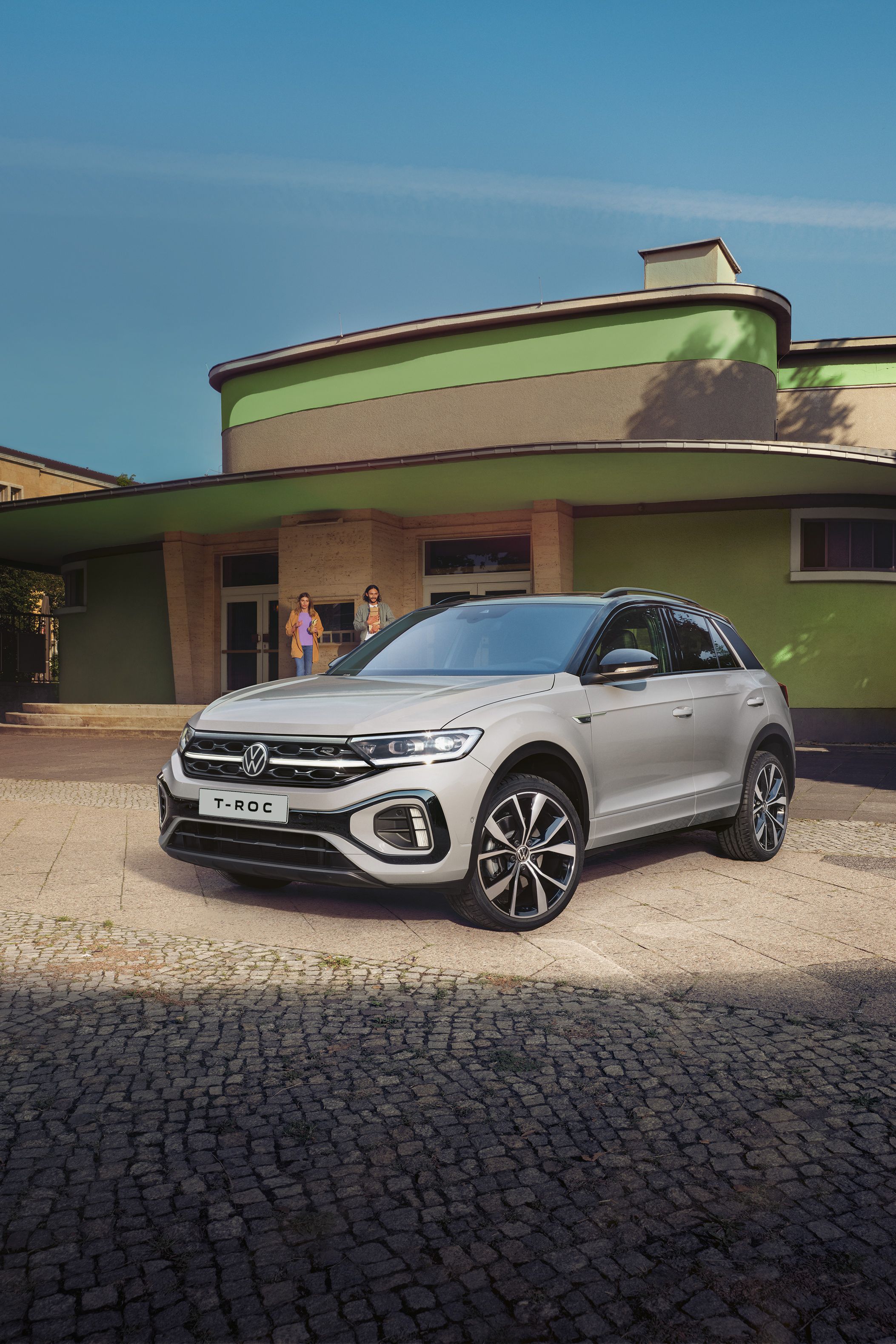 VW T-Roc R-Line in weiß vor einem Gebäude, Front und Seite sichtbar