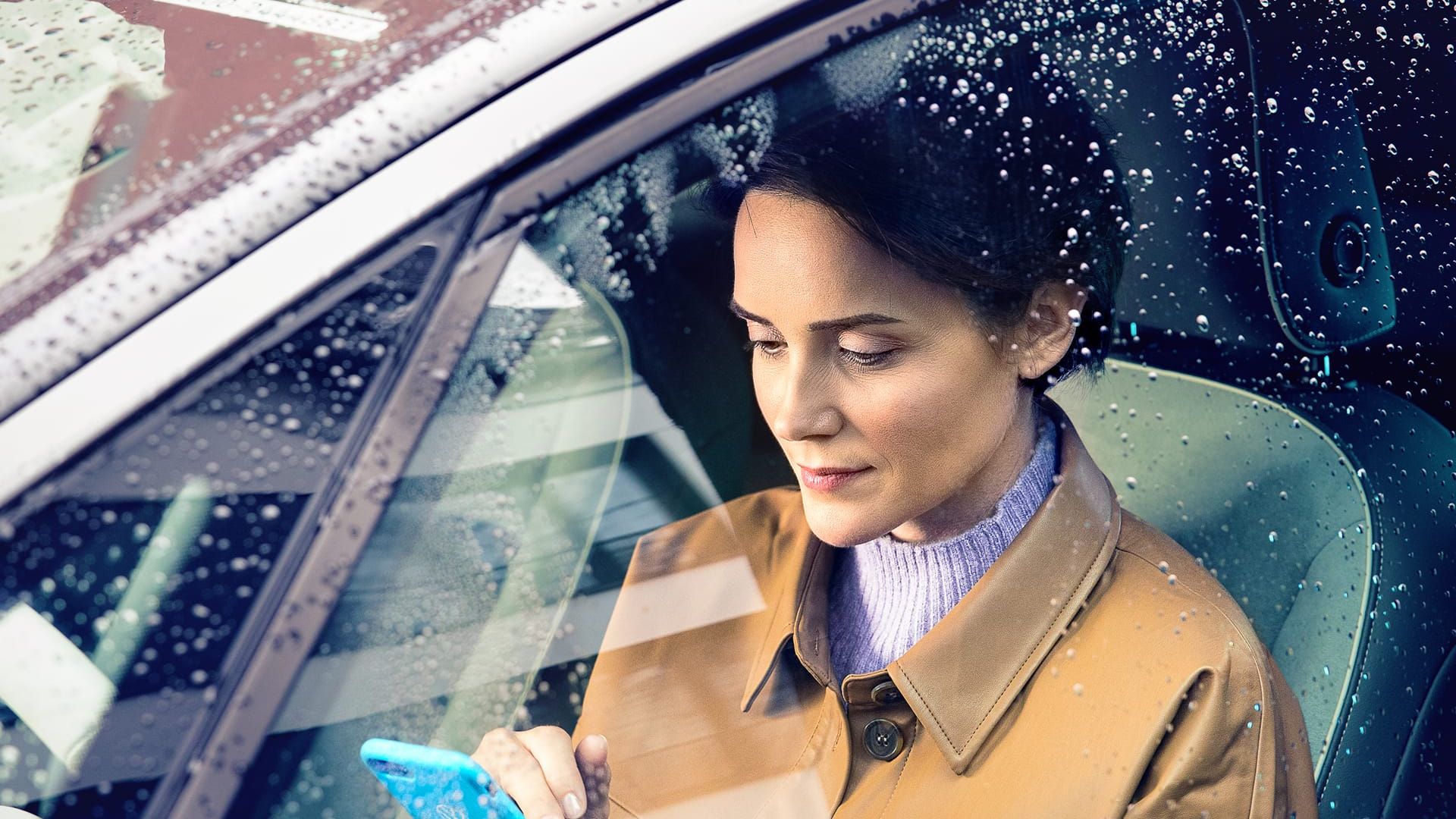 Blick durch Seitenscheibe eines VW ID.3 auf eine Frau, die ein Smartphone bedient.