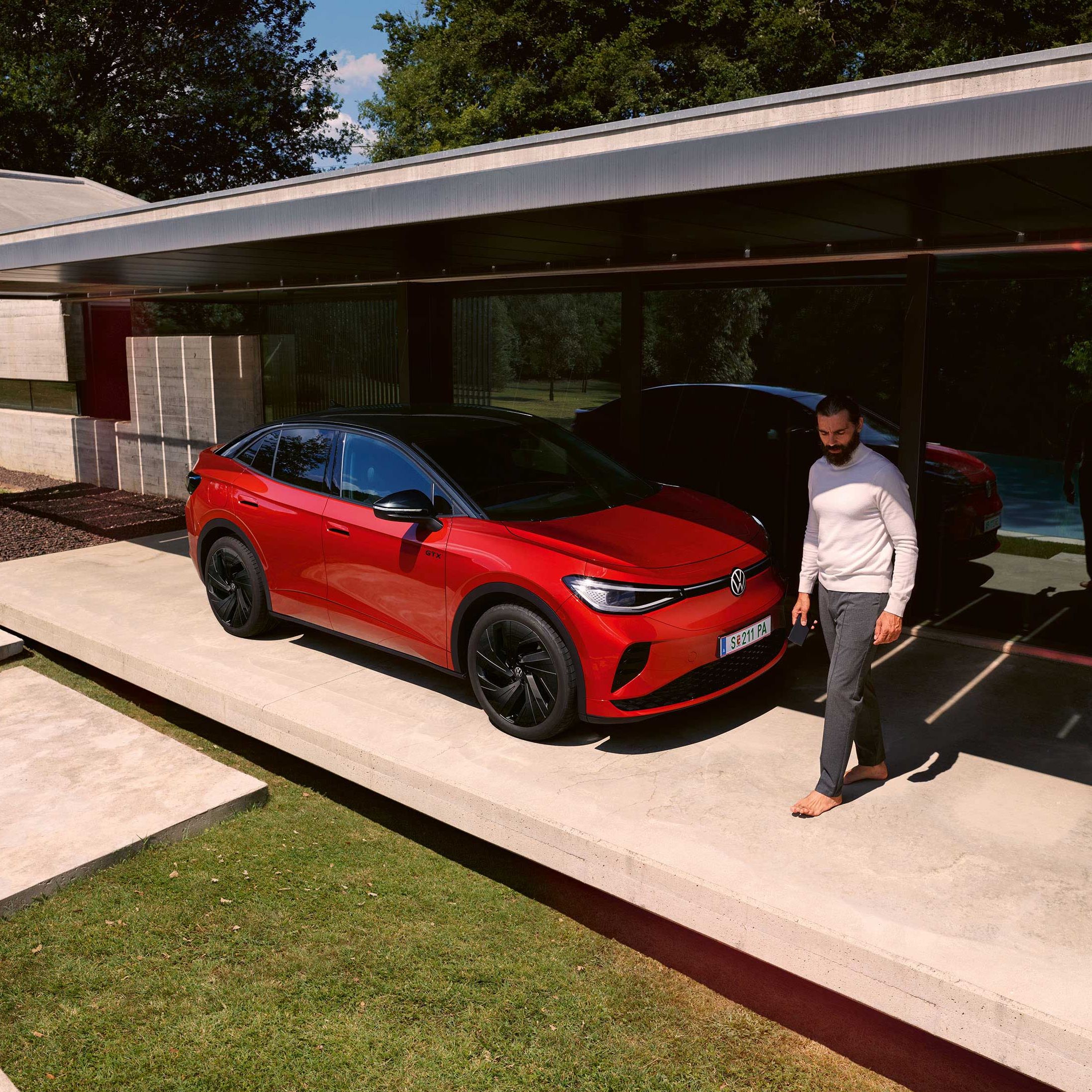 Roter VW ID.5 GTX von schräg vorne in einem modernen Carport, ein Mann geht vor der Motorhaube entlang