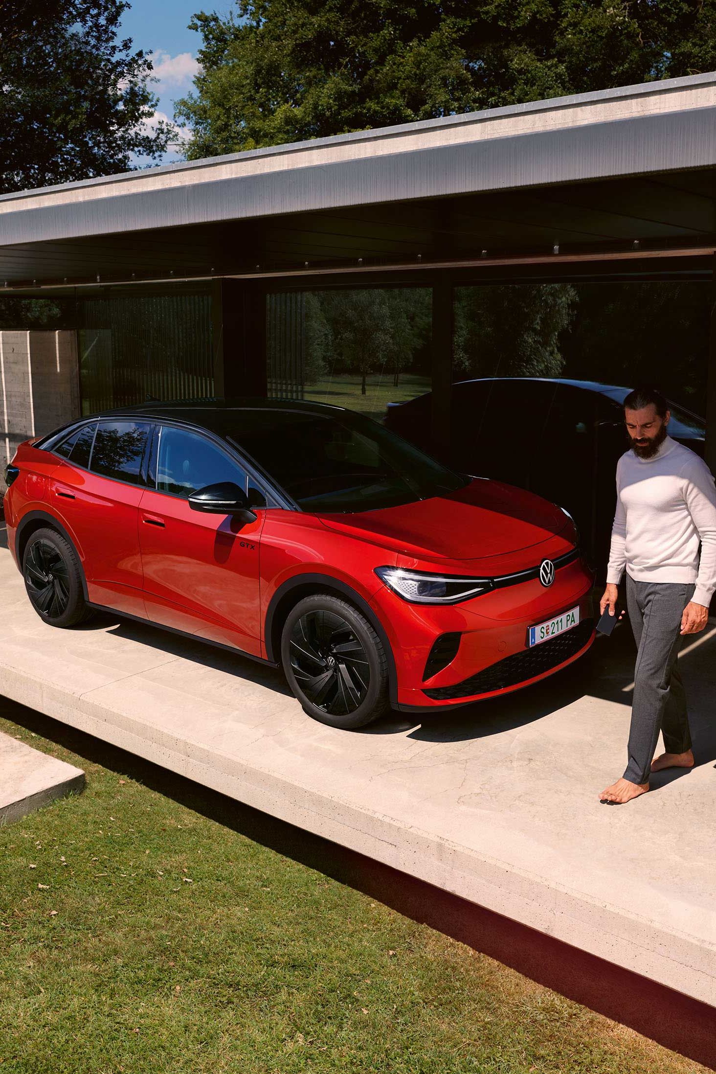 Roter VW ID.5 GTX von schräg vorne in einem modernen Carport, ein Mann geht vor der Motorhaube entlang