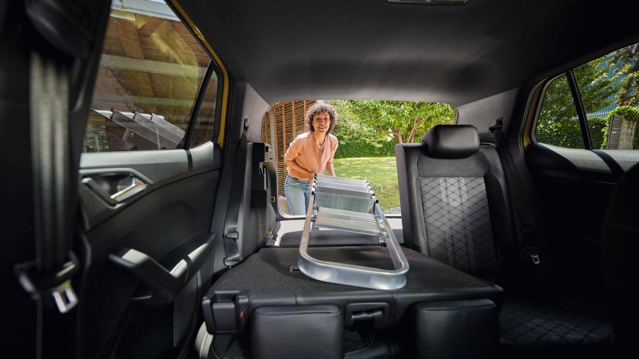 Eine junge Frau schiebt eine Leiter in einen VW T-Cross, über einen umgeklappten Rücksitz.