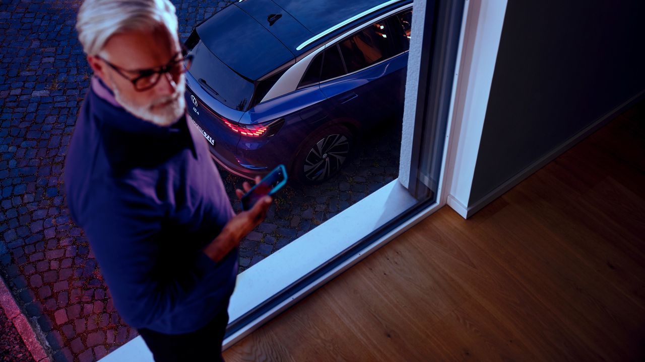 Seitenansicht eines roten VW ID.4 GTX vor Bergkulisse, im Vordergrund blickt eine Frau zum Auto
