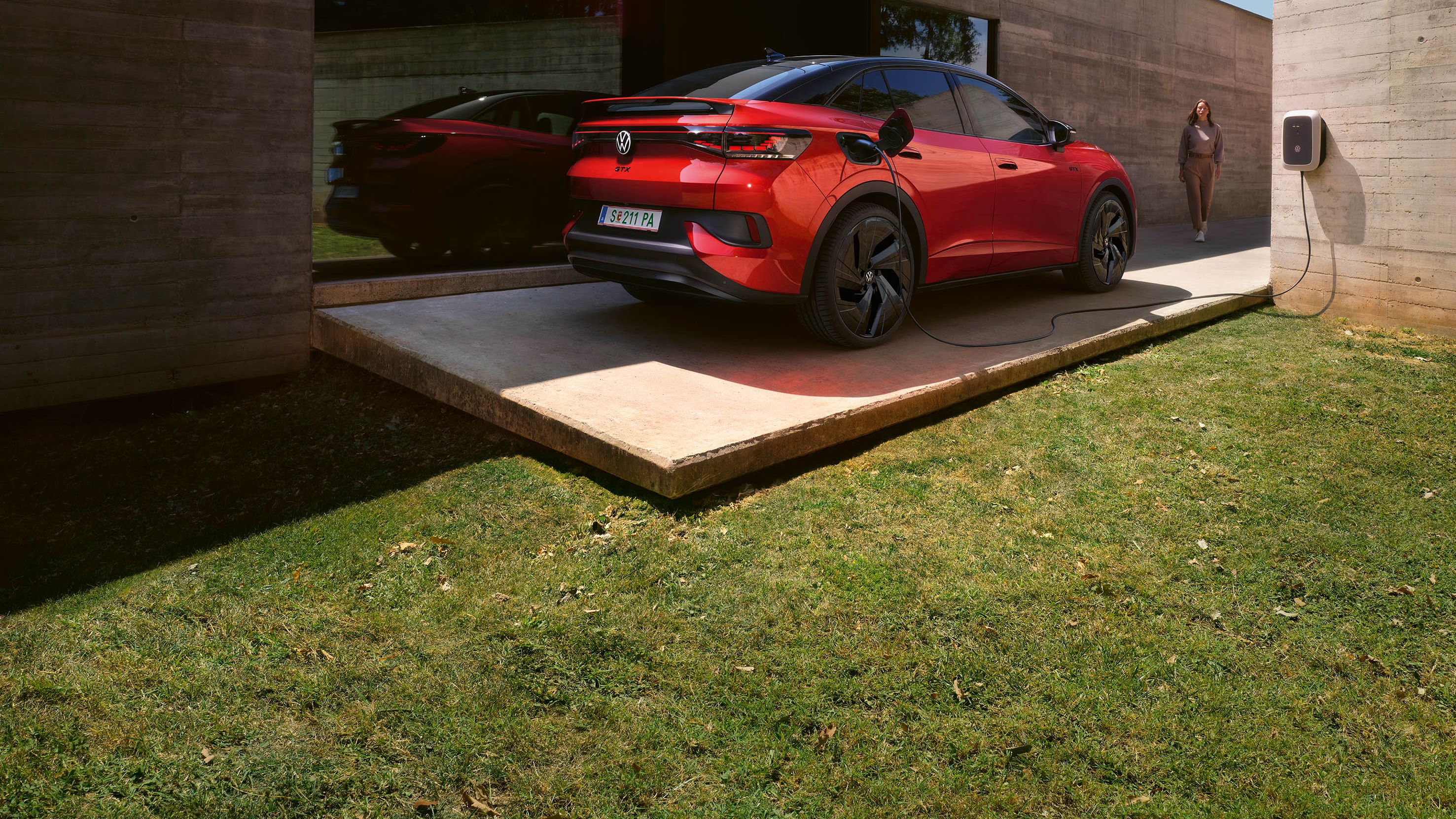 VW ID.5 GTX 4MOTION steht vor einem Haus und lädt Strom, eine Frau geht darauf zu