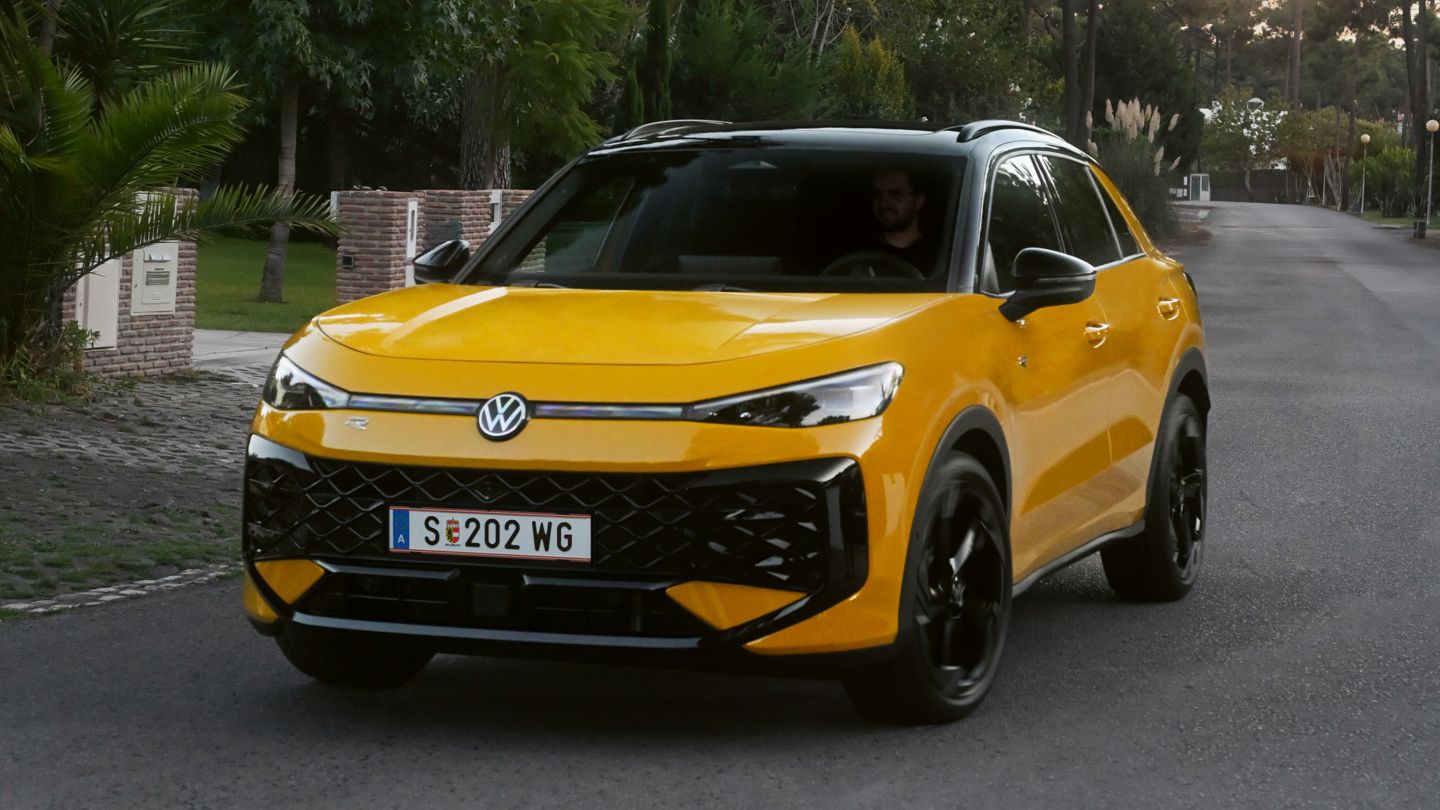 Ein gelber VW T-Roc R-Line fährt auf einer Straße durch eine bewaldete Umgebung.