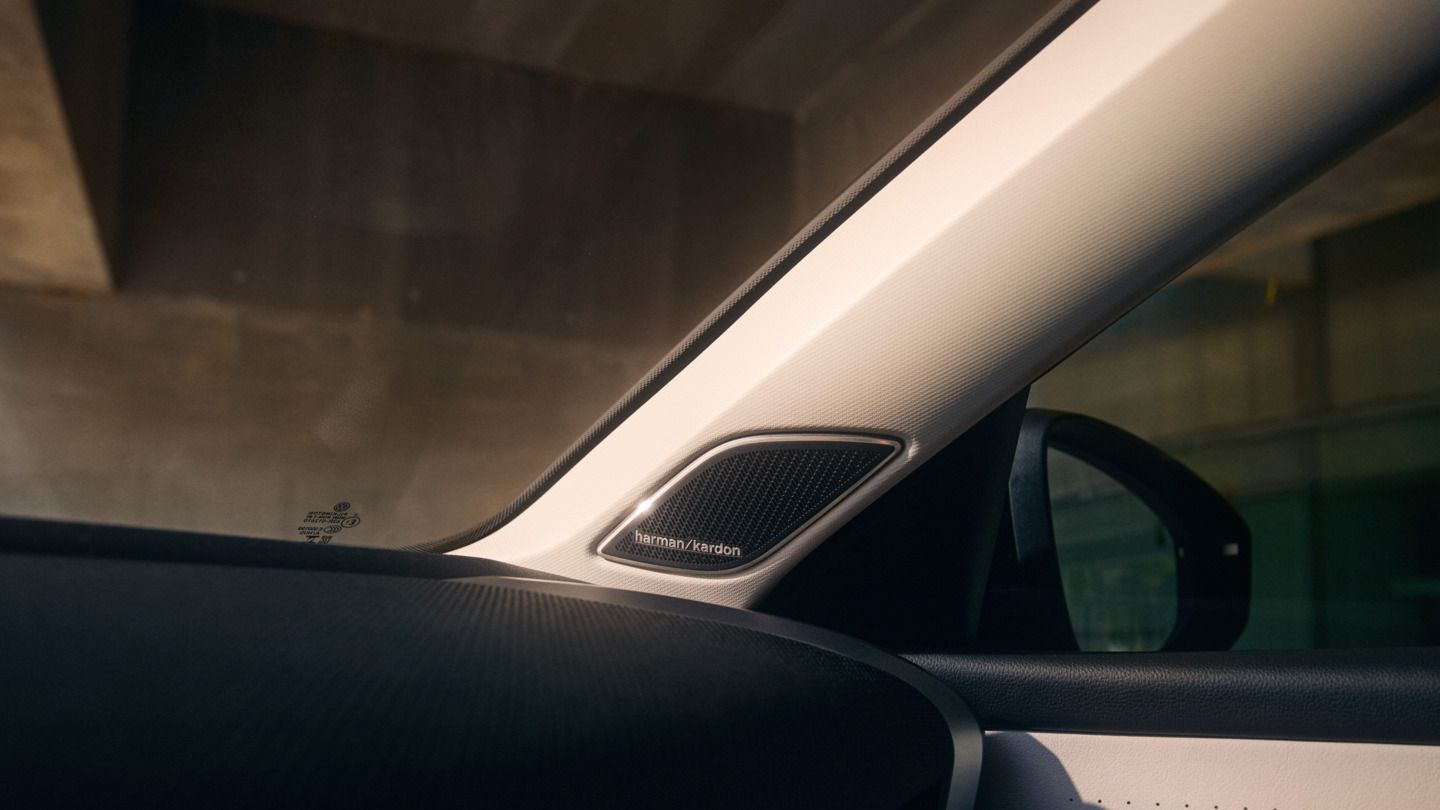 Nahaufnahme des Innenraums eines T-Roc, mit Fokus auf dem Lautsprecher von Harman Kardon in der A-Säule. Man sieht auch einen Teil des Schiebedachs und der Seitenspiegel des Fahrzeugs.
